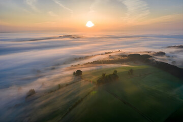 Fototapeta premium Aerial View of Sunrise Over Foggy Green Fields and Trees, High Quality Professional Image