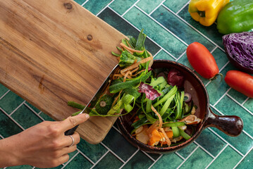 Detailed view of discarded vegetable skins and trimmings on a rustic kitchen surface. Onion layers, carrot ribbons, and zucchini strips in a natural, eco-conscious kitchen with vintage green tiles.