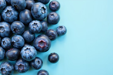 Close-up of fresh blueberries in rich shades of blue and purple scattered on a pastel blue background. Space for text.