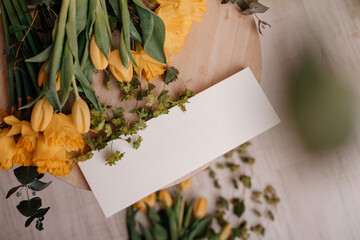 Yellow tulips and blank card on a wooden table, ideal for spring greetings or invitations.