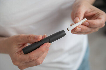 A woman inserts a cigarette stick into a tobacco heating system. Electronic cigarette.