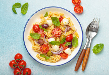 Plate with Italian fusilli pasta salad with fresh cherry tomatoes, mozzarella, olives, red onion, and basil leaves, concept of Italian culinary tradition