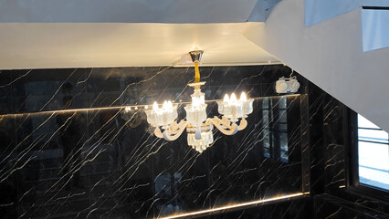 Elegant Crystal Chandelier with Golden Accents Reflected on Glossy Black Marble Wall in Modern Interior Staircase