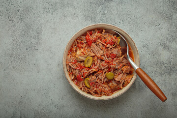 Ropa vieja, a traditional Cuban dish, is served with white rice, tomato sauce, and green olives on a plate from above on grey rustic background, copy space