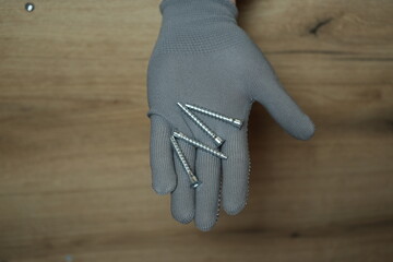 Gray protective glove holding several metal screws for assembling furniture or wooden items.