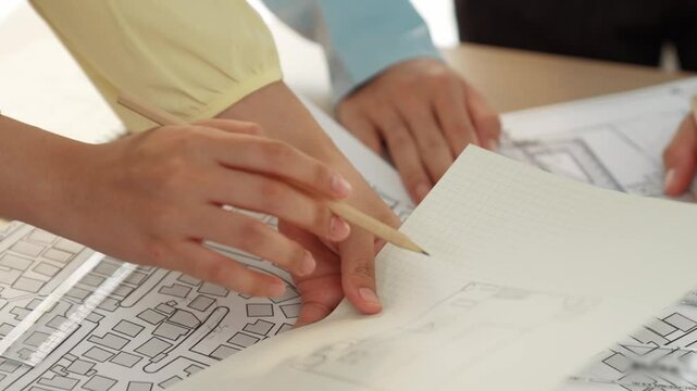 Smart architect and safety engineer discussion about building blueprint on table with architectural document, measurement tools and wooden block scatter around at modern office. Closeup. Delineation.