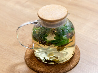Stylish transparent tea pot with just brewed green tea leaves, mint leaves and lemon slices in it....