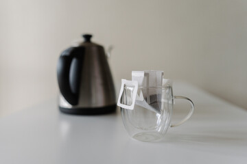 Close-up of drip coffee bag placed in glass cup, ready to brewed with hot water from modern...