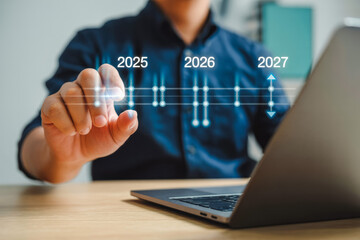 A person interacts with a futuristic timeline interface, highlighting years 2025, 2026 to 2027. They're seated at a desk with a laptop, symbolizing forward-thinking technology and innovation.