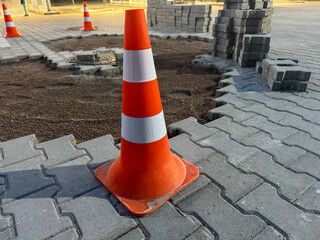 Bright orange safety cones mark an area under construction with newly laid cobblestones and soil,...