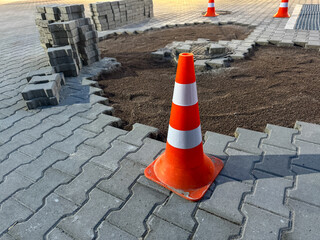 Traffic cones indicate ongoing construction work on a stone pavement. Workers reshape the area, adjusting materials and ensuring public safety during the day