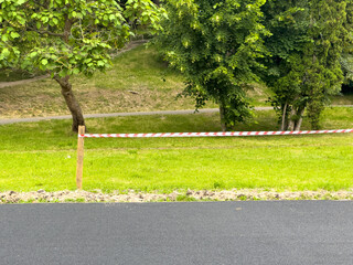 A construction area is divided by red and white warning tape, while a newly paved road glistens in...