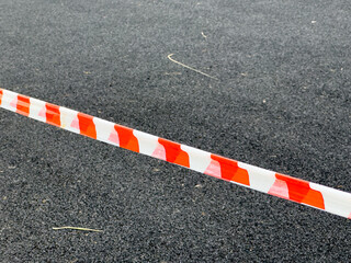 Bright orange and white safety tape stretches across a black asphalt surface, indicating a...