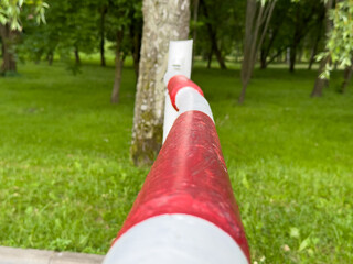 A striking red and white barrier post is positioned in a vibrant green park, surrounded by tall...