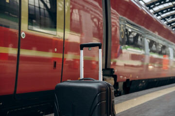 Black suitcase positioned on train platform, with a blurred red train in the background, capturing...