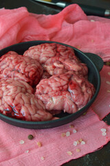 raw animal brains arranged in black frying pan over pink kitchen textile on rustic wooden surface for styled culinary display emphasizing preparation elements and food arrangement techniques.
