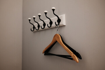 Wooden and plastic clothes hangers hanging on stylish black wall hooks against a gray wall. Simple...