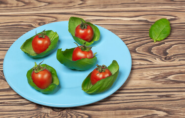 on a wooden background a blue plate with green basil and cherry tomatoes
