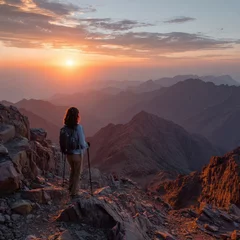 Fototapete Sonnenuntergang Atlas Sunset Trek: A gorgeous woman with trekking poles gazes at the majestic Toubkal Peak during a breathtaking mountain sunset in the Atlas Mountains of North Africa.  © Johannes