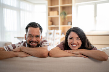 Fototapeta premium Happy couple smiling and leaning on sofa back at home