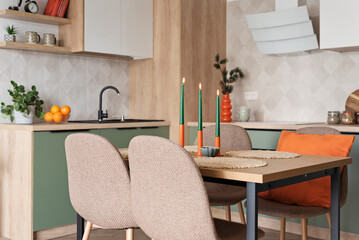 Modern kitchen and wooden dining table with chairs. Green furniture, beige tiles on the wall and orange decoration. New home with elegant design. Real estate.