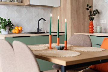 Modern kitchen and wooden dining table with chairs. Green furniture, beige tiles on the wall and orange decoration. New home with elegant design. Real estate.