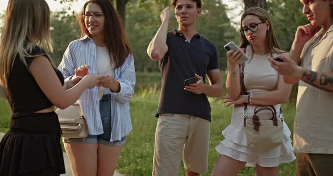 Friends connects in a park, engaging with their mobile phones and sharing laughter. This scene captures modern youth socializing outdoors, balancing digital interaction with natural surroundings.