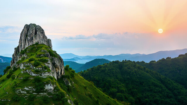 Scenery of a beautiful sunset with a dominant rocky mountain covered in greenery. A distant view of the mountains in the sunlight of the sun and rays. Background, wallpaper.