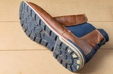Worn black leather men’s shoe with visible sole placed on wooden surface background