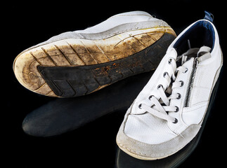Used white men’s shoes with visible wear placed on black studio background