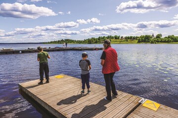 Mother fishing with two sons on wooden pier during sunny day on calm scenic lake. Sweden.