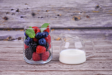 Fresh summer berries with mint in a glass and a jug of milk on a wooden table. Healthy breakfast...