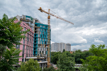Construction crane against the backdrop of urban development, high-rise buildings and trees