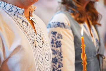 Man and woman in embroidered clothes at ceremony, holding candle with flame, partial view.