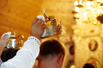 Orthodox wedding ceremony with bride and groom standing, holding candles as crowns are held over...