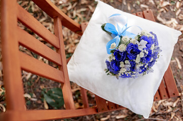 Colorful blue wedding bouquet elegantly arranged with white accents, placed on a pillow on a wooden...