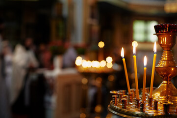 Golden candles burning brightly in a dimly lit church with a priest on blurred background creating a serene and spiritual ambiance.