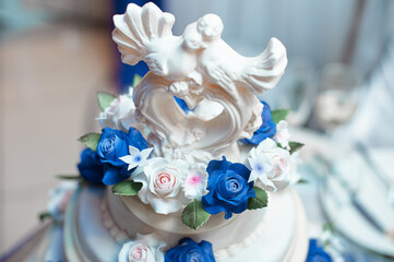 A close-up of a wedding cake adorned with a dove-themed topper surrounded by vibrant blue and white...