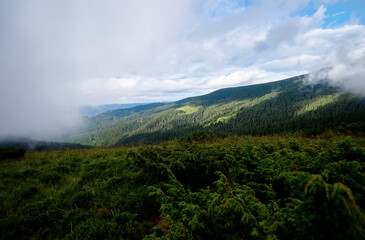 A scenic view of a lush green valley surrounded by forested hills under a partly cloudy sky.