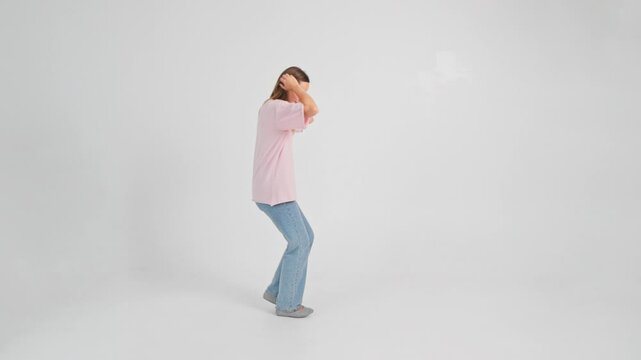 Woman is dancing in moonwalk style moving backwards filmed in studio on white background in slow motion. Young adult Caucasian lady in casual clothes with long hair is going in reverse direction