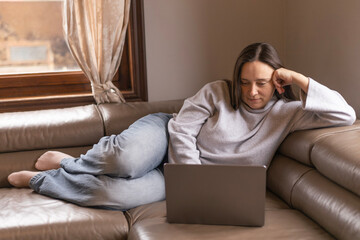 A woman watches a movie on her laptop while lying on the couch