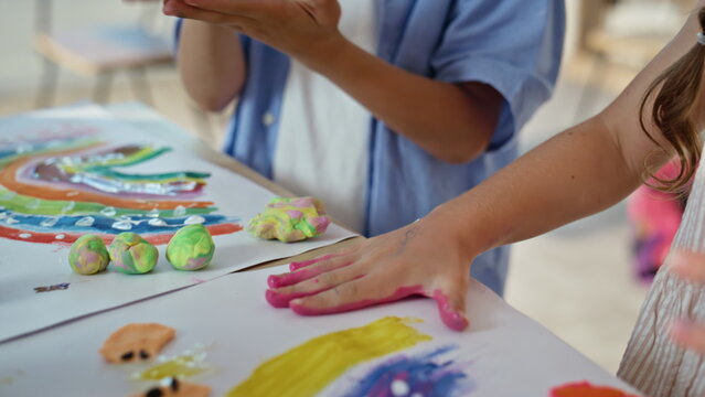 School girl painting hand creating palm prints on paper closeup. Happy child 