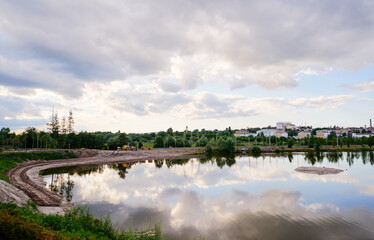 Serene Landscaped Lake With Reflection and Nearby Urban Skyline Under a Cloudy Sky