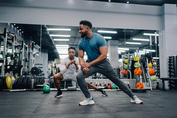 Two male athletes stretching legs in modern gym