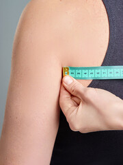 A detail image showcasing a hand measuring the circumference of an upper arm using a tape measure....