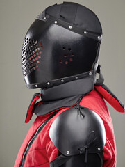 Close-up of person wearing black and red armor with protective helmet, shoulder guards, and padded...