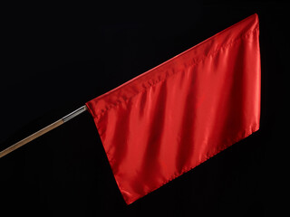 A vivid red flag attached to a wooden stick, isolated against a dark black background, symbolizing...