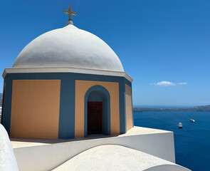 Iconic Greek church with white dome and blue walls perched above the sea