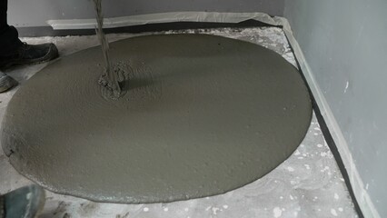 Construction worker pouring and spreading self-leveling concrete on floor.