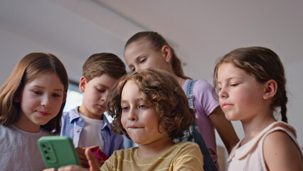 Schoolmates playing mobile phone together closeup. Smiling elementary pupils